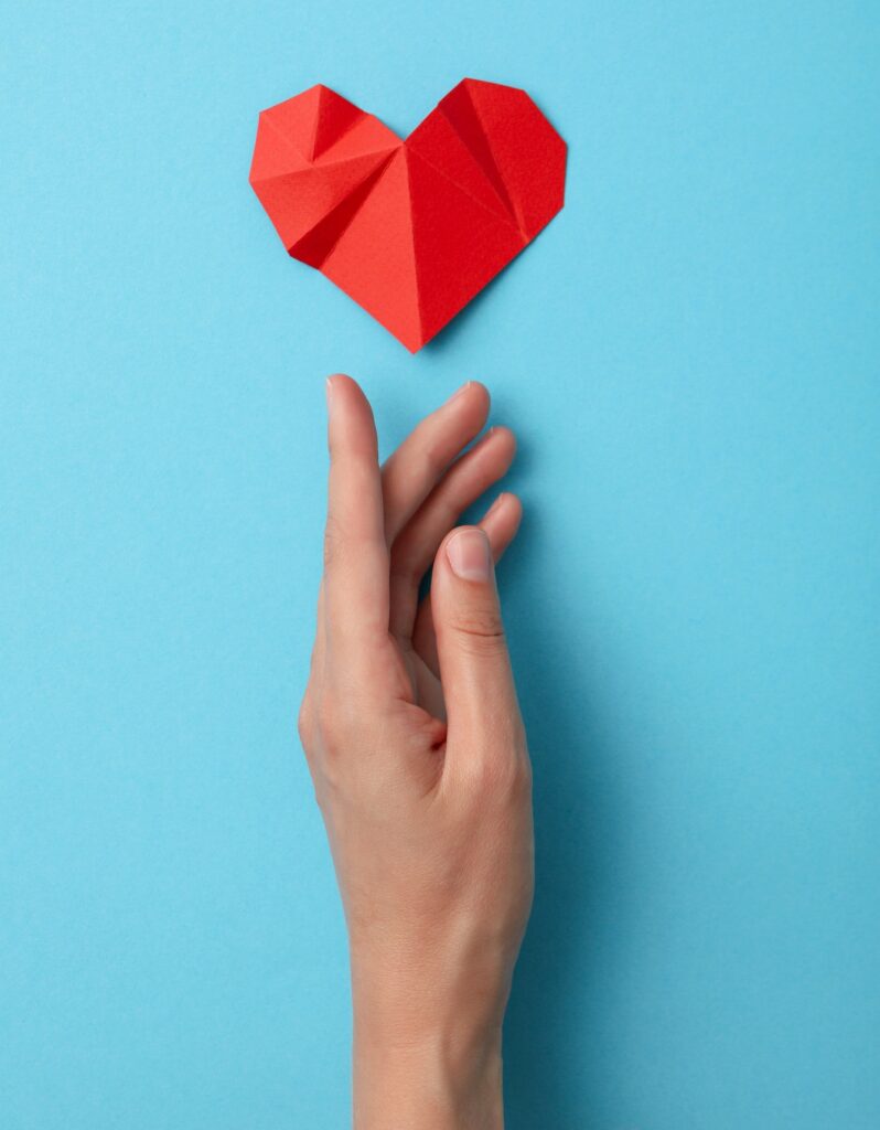 Red paper heart with a hand on a blue background. Blood donation